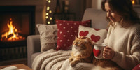Une femme assise confortablement sur un canapé caresse un chat roux près d'une cheminée allumée, avec une tasse à motif cœur et une ambiance chaleureuse de Saint-Valentin.