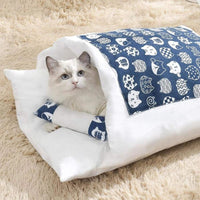 Chat blanc confortablement installé dans une couette fermée douce et élégante, motif bleu avec têtes de chat.