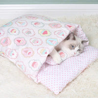 Chat blanc regardant autour depuis une couette fermée rose et douce, ornée de motifs colorés, idéale pour l'hiver.