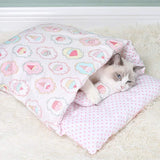 Chat blanc regardant autour depuis une couette fermée rose et douce, ornée de motifs colorés, idéale pour l'hiver.